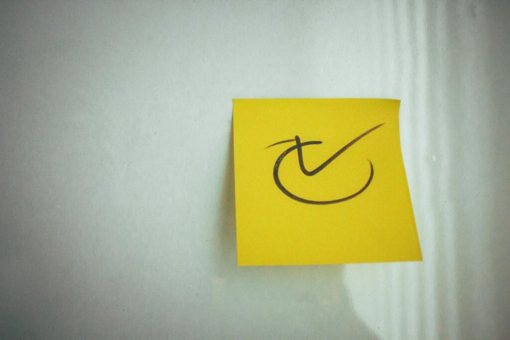 Yellow sticky note with a check mark symbol on a white background, ideal for reminders.